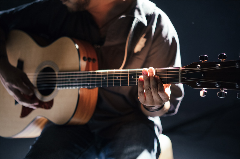 Das Bild zeigt einen Mann der eine Aktustikgitarre spielt und dient als Beitragsbild zur musikalischen Veranstaltung Sunday Lunch im Hotel Restaurant Fliegerheim in Borkheide bei Beelitz in Brandenburg.